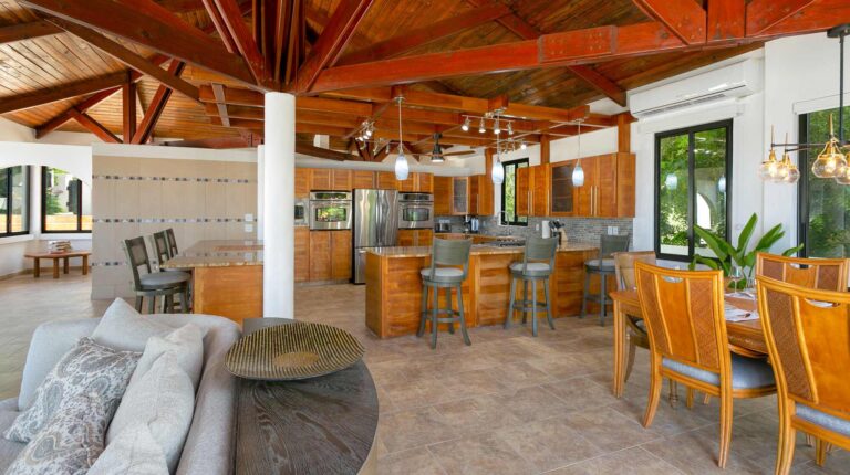 Open-plan great room with a vaulted timber cathedral ceiling and a central column, joining a gray sofa lounge, the kitchen and dining areas.
