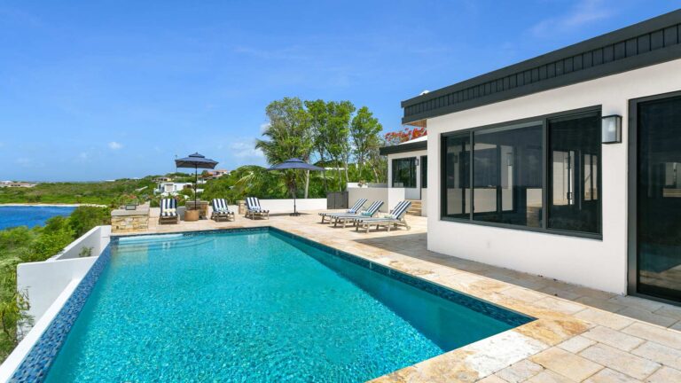 Long infinity pool on a travertine deck with sun loungers and umbrellas, beside the villa and overlooking the bay.