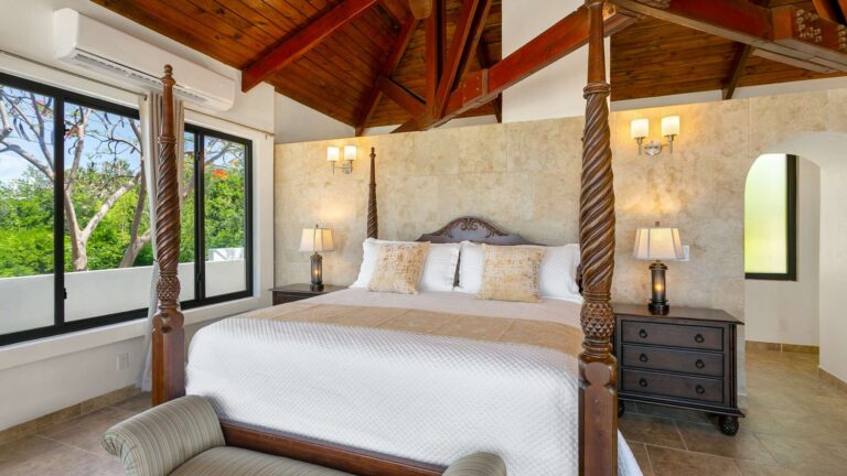 Bedroom with a carved four-poster bed against a stone accent wall, wall sconces, matching lamp-topped nightstands and a garden window.