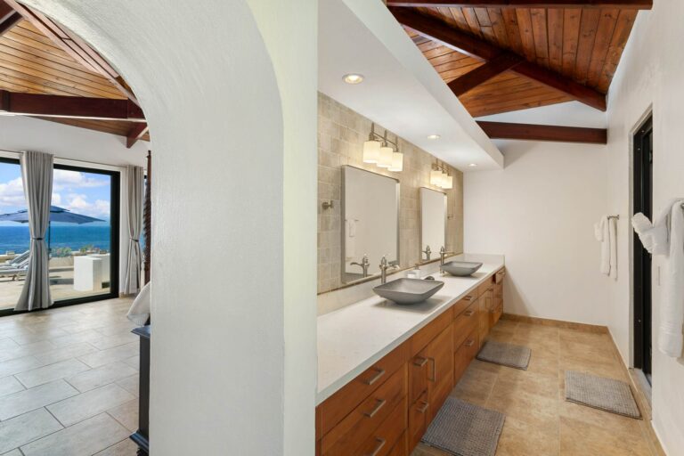 Master bathroom with a double vanity and stone vessel sinks, travertine tile and an archway opening to the bedroom and an ocean-view terrace.