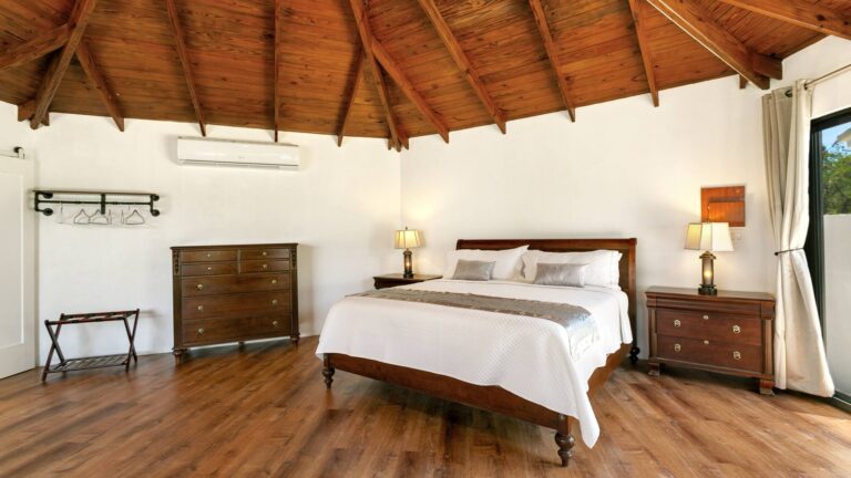 Bedroom with a vaulted timber ceiling and wood floor, a mahogany sleigh bed, dresser, two lamp-topped nightstands and a luggage rack.